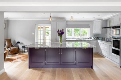 Mid-sized elegant medium tone wood floor and brown floor kitchen photo in Wiltshire with an undermount sink, shaker cabinets, gray cabinets, granite countertops, gray backsplash, stainless steel appliances and gray countertops