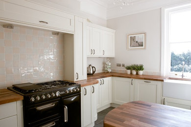This is an example of a medium sized traditional u-shaped enclosed kitchen in Surrey with a belfast sink, shaker cabinets, white cabinets, wood worktops, ceramic splashback, slate flooring, a breakfast bar and black floors.