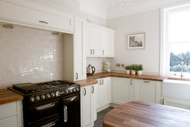 Inspiration for a mid-sized timeless u-shaped slate floor and black floor enclosed kitchen remodel in Surrey with a farmhouse sink, shaker cabinets, white cabinets, wood countertops, ceramic backsplash and a peninsula