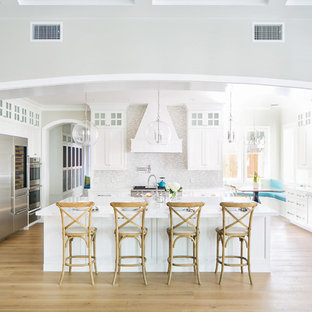 Transitional eat-in kitchen inspiration - Example of a transitional light wood floor and beige floor eat-in kitchen design in Orange County with a farmhouse sink, shaker cabinets, white cabinets, gray backsplash, stainless steel appliances, an island and white countertops
