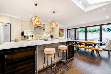 This is an example of a medium sized single-wall kitchen/diner in London with a single-bowl sink, shaker cabinets, beige cabinets, quartz worktops, ceramic splashback, integrated appliances, dark hardwood flooring, an island, brown floors and white worktops.