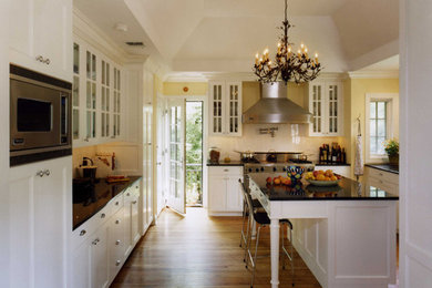 Example of a large classic medium tone wood floor eat-in kitchen design in New York with recessed-panel cabinets, white cabinets, marble countertops, stainless steel appliances and an island