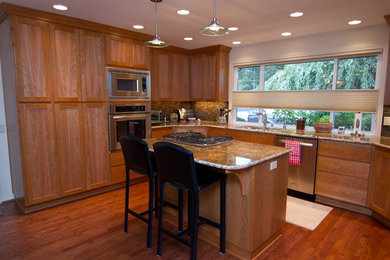 Example of a large classic u-shaped medium tone wood floor eat-in kitchen design in Portland with an undermount sink, shaker cabinets, medium tone wood cabinets, granite countertops, multicolored backsplash, stone tile backsplash, stainless steel appliances and an island