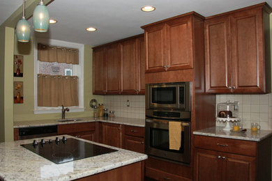 Example of a classic l-shaped dark wood floor eat-in kitchen design in Philadelphia with an undermount sink, raised-panel cabinets, medium tone wood cabinets, granite countertops, beige backsplash, ceramic backsplash, stainless steel appliances and an island