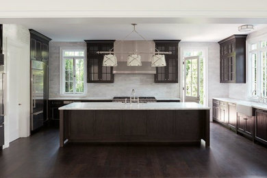 Inspiration for a transitional u-shaped medium tone wood floor and brown floor kitchen remodel in Los Angeles with a farmhouse sink, beaded inset cabinets, dark wood cabinets, marble countertops, white backsplash, marble backsplash, stainless steel appliances, an island and white countertops