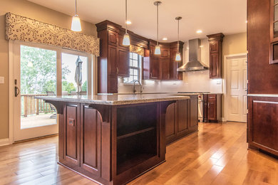 Eat-in kitchen - traditional u-shaped light wood floor and brown floor eat-in kitchen idea in Chicago with a drop-in sink, raised-panel cabinets, dark wood cabinets, granite countertops, white backsplash, glass tile backsplash, stainless steel appliances, an island and brown countertops