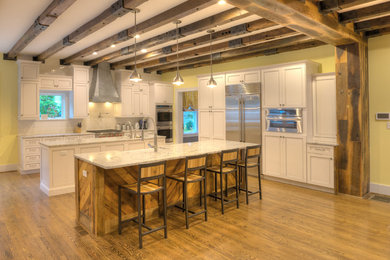 Example of a large cottage l-shaped medium tone wood floor and brown floor eat-in kitchen design in Other with a farmhouse sink, recessed-panel cabinets, white cabinets, marble countertops, white backsplash, ceramic backsplash, stainless steel appliances and two islands