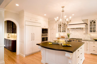 Inspiration for a mid-sized timeless u-shaped light wood floor enclosed kitchen remodel in Boston with an undermount sink, beaded inset cabinets, white cabinets, paneled appliances, an island, gray backsplash and subway tile backsplash