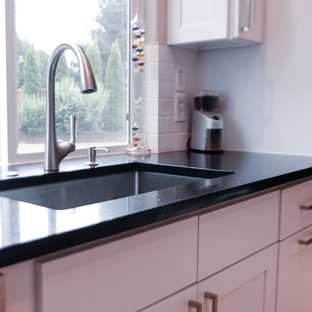 Inspiration for a mid-sized traditional u-shaped eat-in kitchen in Seattle with shaker cabinets, granite benchtops, white splashback, ceramic splashback, stainless steel appliances, light hardwood floors, black benchtop, an integrated sink, white cabinets and with island.