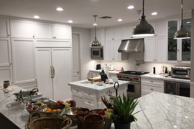 Mid-sized transitional u-shaped dark wood floor kitchen photo in Miami with a farmhouse sink, shaker cabinets, white cabinets, marble countertops, white backsplash, subway tile backsplash, stainless steel appliances and an island