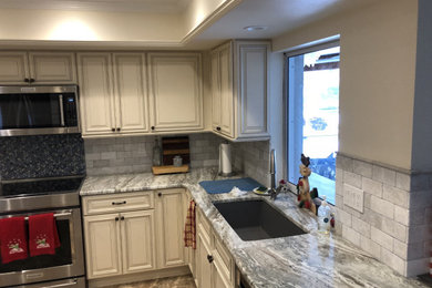 Inspiration for a mid-sized timeless u-shaped porcelain tile, gray floor and tray ceiling enclosed kitchen remodel in Other with a drop-in sink, white cabinets, gray backsplash, ceramic backsplash, stainless steel appliances, gray countertops, granite countertops, no island and raised-panel cabinets
