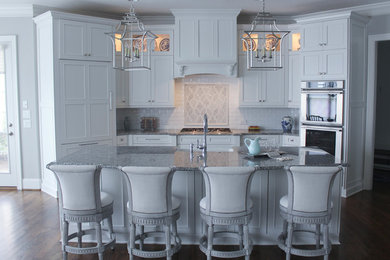 Exempel på ett mellanstort klassiskt kök, med en rustik diskho, luckor med infälld panel, vita skåp, granitbänkskiva, vitt stänkskydd, stänkskydd i stenkakel, integrerade vitvaror, mellanmörkt trägolv och en köksö