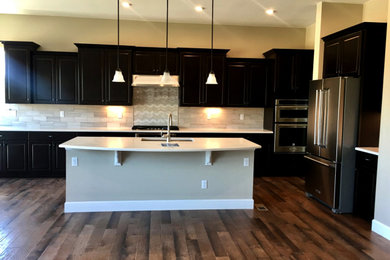 Medium tone wood floor and brown floor kitchen photo in Denver with a single-bowl sink, raised-panel cabinets, dark wood cabinets, quartz countertops, limestone backsplash, stainless steel appliances, an island and white countertops
