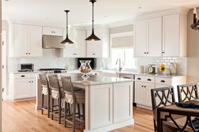 Example of a mid-sized transitional l-shaped light wood floor and beige floor eat-in kitchen design in Boston with recessed-panel cabinets, white cabinets, granite countertops, white backsplash, subway tile backsplash, stainless steel appliances, an island and a farmhouse sink
