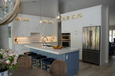 This is an example of a medium sized coastal l-shaped kitchen/diner in Miami with a submerged sink, raised-panel cabinets, white cabinets, engineered stone countertops, blue splashback, marble splashback, stainless steel appliances, porcelain flooring, an island and grey floors.