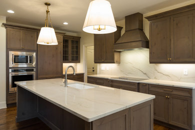 Imagen de cocina comedor lineal tradicional renovada de tamaño medio con fregadero de un seno, armarios estilo shaker, puertas de armario de madera en tonos medios, encimera de granito, salpicadero blanco, salpicadero de losas de piedra, electrodomésticos con paneles, suelo de madera oscura, una isla, suelo marrón y encimeras blancas