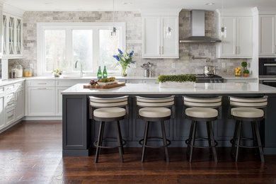 Inspiration for a large transitional l-shaped dark wood floor and brown floor kitchen remodel in Other with white cabinets, quartz countertops, gray backsplash, stainless steel appliances, an island, an undermount sink, shaker cabinets and stone tile backsplash