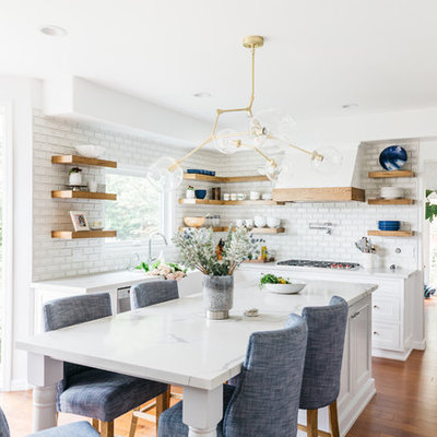 Inspiration for a mid-sized transitional u-shaped medium tone wood floor and brown floor eat-in kitchen remodel in Los Angeles with a farmhouse sink, recessed-panel cabinets, white cabinets, quartzite countertops, white backsplash, subway tile backsplash, stainless steel appliances, an island and white countertops