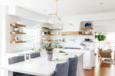 Example of a mid-sized transitional u-shaped medium tone wood floor and brown floor eat-in kitchen design in Los Angeles with a farmhouse sink, recessed-panel cabinets, white cabinets, quartzite countertops, white backsplash, subway tile backsplash, stainless steel appliances, an island and white countertops