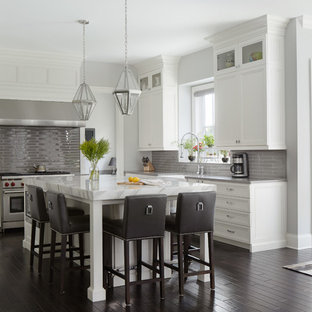 Ejemplo de cocina comedor clásica renovada con armarios con paneles empotrados, puertas de armario blancas, salpicadero verde, electrodomésticos de acero inoxidable, suelo de madera oscura y una isla