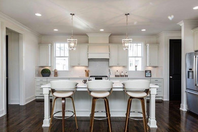 Inspiration for a large transitional l-shaped dark wood floor kitchen remodel in Raleigh with an undermount sink, recessed-panel cabinets, white cabinets, solid surface countertops, white backsplash, ceramic backsplash, stainless steel appliances and an island