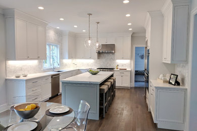 This is an example of a large classic u-shaped open plan kitchen in New York with a submerged sink, white cabinets, marble worktops, white splashback, marble splashback, stainless steel appliances, medium hardwood flooring, an island, brown floors and recessed-panel cabinets.