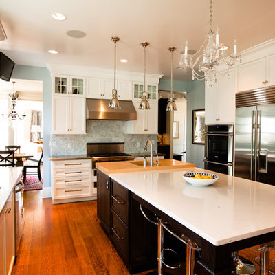Example of a mid-sized classic u-shaped medium tone wood floor eat-in kitchen design in Chicago with recessed-panel cabinets, a double-bowl sink, white cabinets, quartz countertops, stainless steel appliances, gray backsplash and an island