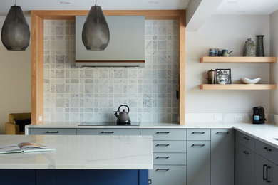 Photo of a medium sized classic u-shaped open plan kitchen in Edmonton with a double-bowl sink, flat-panel cabinets, grey cabinets, engineered stone countertops, blue splashback, marble splashback, black appliances, medium hardwood flooring, an island and brown floors.