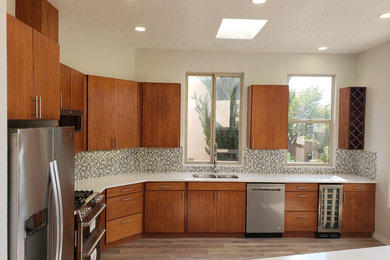Kitchen - large transitional l-shaped medium tone wood floor and brown floor kitchen idea in Albuquerque with an undermount sink, flat-panel cabinets, medium tone wood cabinets, solid surface countertops, multicolored backsplash, glass tile backsplash, stainless steel appliances, an island and white countertops