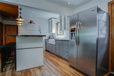 Inspiration for a mid-sized transitional galley medium tone wood floor kitchen remodel in Grand Rapids with a farmhouse sink, shaker cabinets, white cabinets, granite countertops, white backsplash, subway tile backsplash, stainless steel appliances and a peninsula