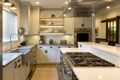 Mid-sized transitional l-shaped medium tone wood floor and brown floor eat-in kitchen photo in Boston with a farmhouse sink, shaker cabinets, white cabinets, white backsplash, subway tile backsplash, stainless steel appliances and an island