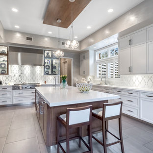 Imagen de cocina comedor en U, clásica renovada, de tamaño medio, con armarios con paneles empotrados, puertas de armario blancas, salpicadero blanco, electrodomésticos de acero inoxidable, una isla, fregadero bajoencimera, encimera de acrílico, suelo de baldosas de porcelana y salpicadero con mosaicos de azulejos