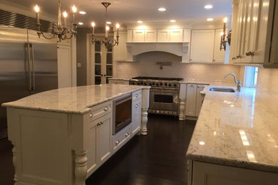 Example of a transitional u-shaped dark wood floor kitchen design in New York with an undermount sink, recessed-panel cabinets, white cabinets, granite countertops, white backsplash, subway tile backsplash, stainless steel appliances and an island
