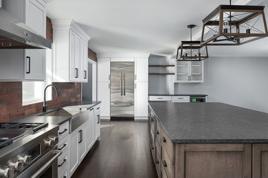 Example of a large transitional u-shaped dark wood floor and brown floor eat-in kitchen design in Chicago with white cabinets, stainless steel appliances, an island, a farmhouse sink, recessed-panel cabinets, soapstone countertops, red backsplash, brick backsplash and black countertops