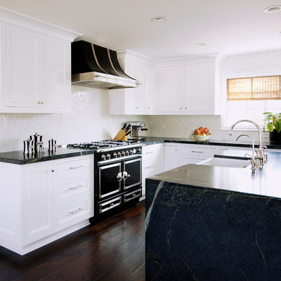 Example of a mid-sized transitional u-shaped dark wood floor and brown floor enclosed kitchen design in Austin with a farmhouse sink, recessed-panel cabinets, white cabinets, soapstone countertops, white backsplash, stainless steel appliances, an island and marble backsplash