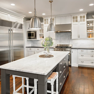 Inspiration for a mid-sized transitional u-shaped dark wood floor kitchen remodel in San Francisco with a farmhouse sink, shaker cabinets, white cabinets, marble countertops, white backsplash, stainless steel appliances, an island and stone tile backsplash