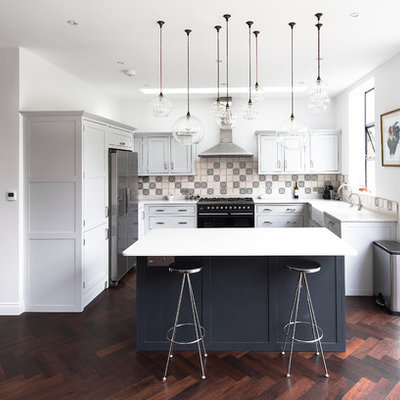 Example of a mid-sized transitional dark wood floor open concept kitchen design in London with a farmhouse sink, shaker cabinets, gray cabinets, quartzite countertops, ceramic backsplash, stainless steel appliances and an island