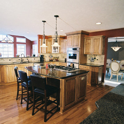 Example of a large transitional u-shaped medium tone wood floor and brown floor kitchen design in Cleveland with an undermount sink, raised-panel cabinets, light wood cabinets, granite countertops, beige backsplash, ceramic backsplash, stainless steel appliances and an island