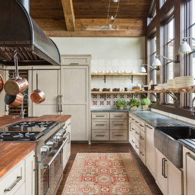 Eat-in kitchen - large rustic u-shaped medium tone wood floor, brown floor and wood ceiling eat-in kitchen idea in Houston with a farmhouse sink, shaker cabinets, beige cabinets, soapstone countertops, white backsplash, porcelain backsplash, stainless steel appliances, an island and gray countertops