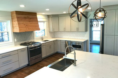 Mid-sized transitional dark wood floor and brown floor open concept kitchen photo in Birmingham with a farmhouse sink, shaker cabinets, white cabinets, quartzite countertops, white backsplash, subway tile backsplash, stainless steel appliances and an island
