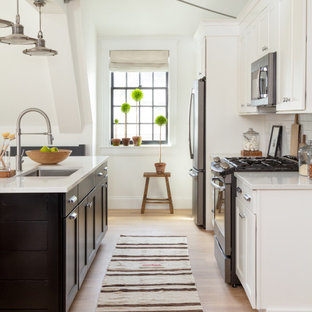 Transitional kitchen pictures - Example of a transitional galley medium tone wood floor and brown floor kitchen design in Boston with an undermount sink, shaker cabinets, white cabinets, stainless steel appliances, an island and white countertops