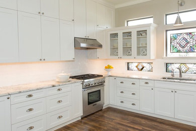 Large transitional l-shaped medium tone wood floor and multicolored floor kitchen pantry photo in Houston with an undermount sink, shaker cabinets, white cabinets, granite countertops, white backsplash, glass tile backsplash, stainless steel appliances and no island
