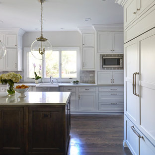 Transitional kitchen designs - Transitional dark wood floor kitchen photo in Chicago with a farmhouse sink, beaded inset cabinets, white cabinets, quartz countertops, white backsplash, stone tile backsplash, paneled appliances and an island