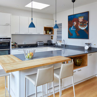 Classic u-shaped kitchen in London with a submerged sink, flat-panel cabinets, white cabinets, stainless steel appliances, medium hardwood flooring, brown floors and grey worktops.