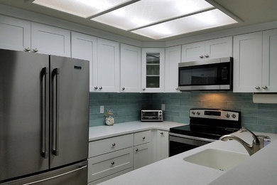 Example of a small transitional u-shaped medium tone wood floor, brown floor and tray ceiling enclosed kitchen design in Orange County with an integrated sink, shaker cabinets, white cabinets, quartz countertops, green backsplash, glass tile backsplash, stainless steel appliances, no island and white countertops