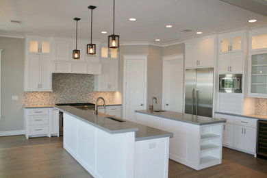 Example of a large transitional l-shaped light wood floor and brown floor open concept kitchen design in Houston with an undermount sink, shaker cabinets, white cabinets, quartzite countertops, multicolored backsplash, mosaic tile backsplash, stainless steel appliances and two islands