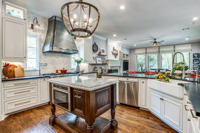 Inspiration for a mid-sized transitional u-shaped medium tone wood floor kitchen remodel in Dallas with a farmhouse sink, recessed-panel cabinets, white cabinets, white backsplash, stainless steel appliances, an island, black countertops, granite countertops and marble backsplash