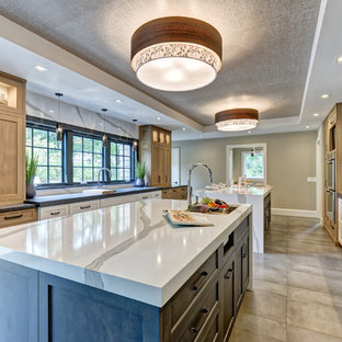 Large transitional galley eat-in kitchen in New York with an undermount sink, shaker cabinets, grey cabinets, quartz benchtops, white splashback, stone slab splashback, stainless steel appliances, porcelain floors, multiple islands, brown floor and white benchtop.
