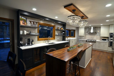 Example of a mid-sized transitional u-shaped dark wood floor eat-in kitchen design in Chicago with an undermount sink, flat-panel cabinets, gray backsplash, white cabinets, solid surface countertops, stone tile backsplash, stainless steel appliances and an island
