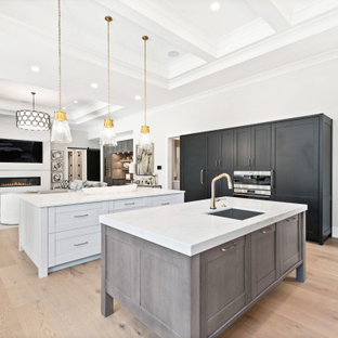 Idées déco pour une très grand cuisine classique en U avec un évier encastré, un placard à porte shaker, des portes de placard grises, un plan de travail en quartz modifié, une crédence blanche, une crédence en quartz modifié, un électroménager en acier inoxydable, un sol en bois clair, 2 îlots, un sol marron, un plan de travail blanc et un plafond à caissons.